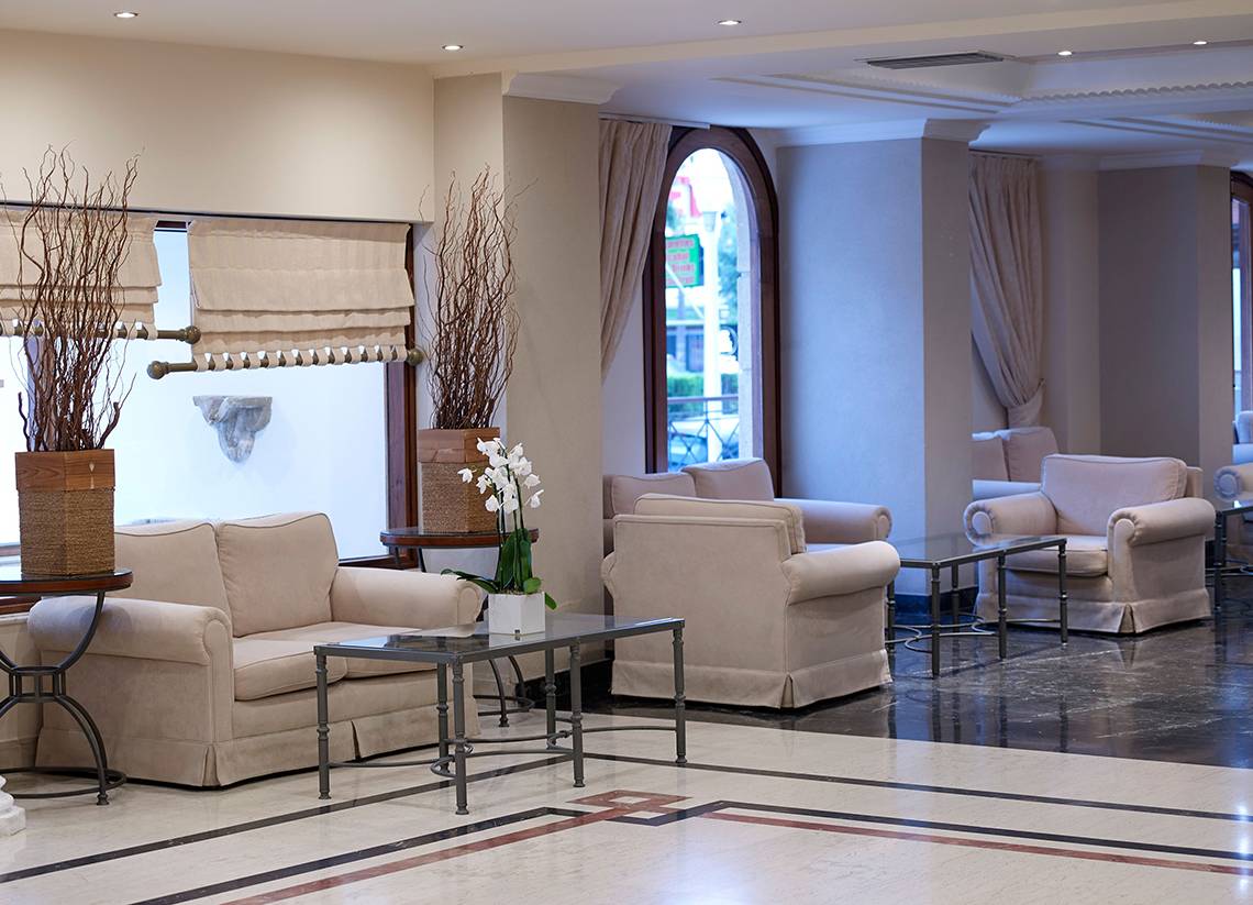 Lobby des Mitsis Petit Palais Beach Hotels mit beige Möbeln und großen Fenstern.