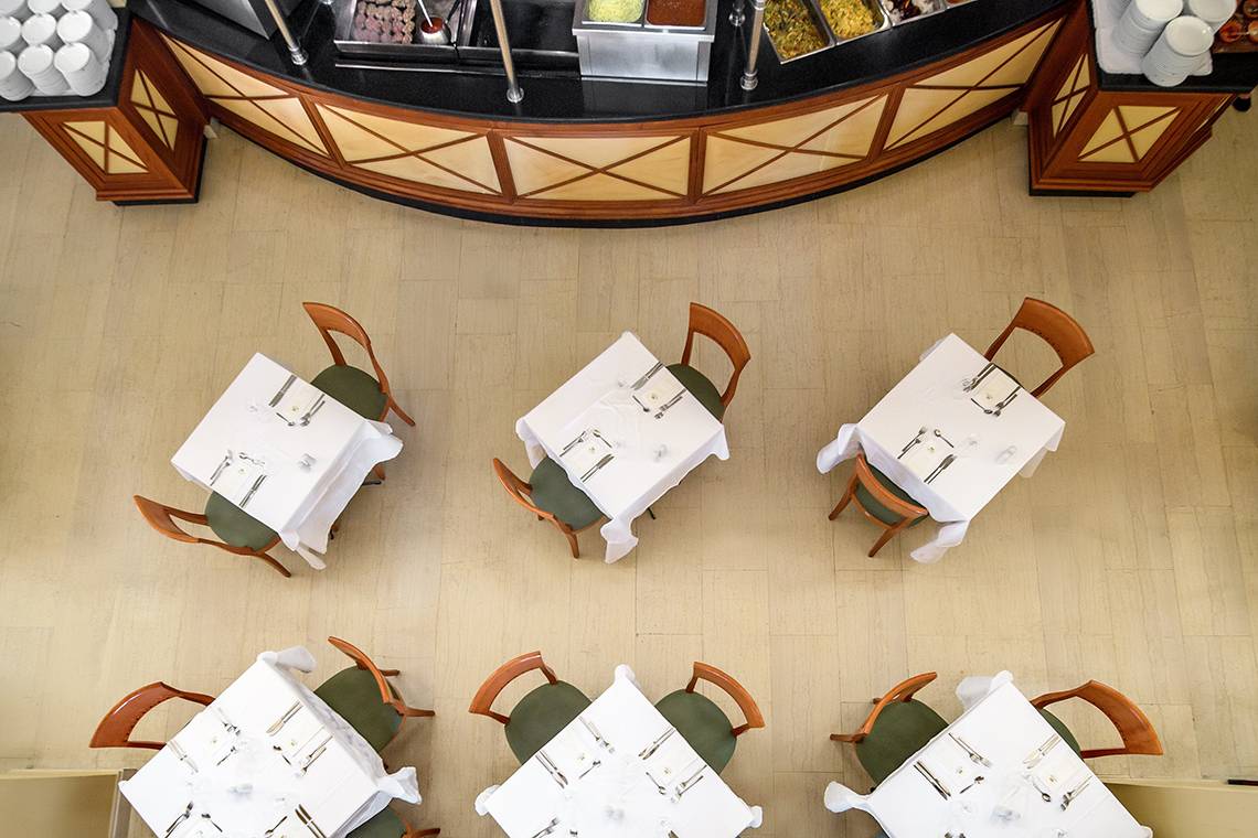 Oberansicht des Speisebereichs im Mitsis Petit Palais Beach Hotel mit fünf gedeckten Tischen und einer Theke im Hintergrund.
