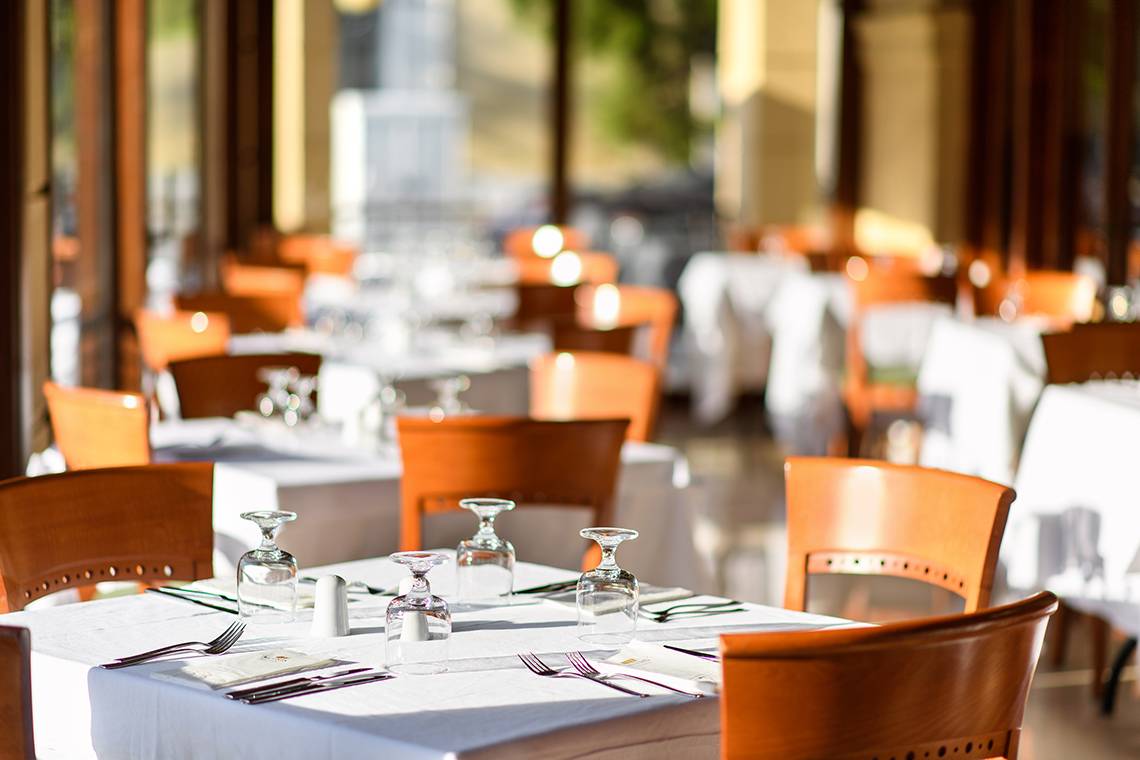 Restauranttisch im Mitsis Petit Palais Beach Hotel, gedeckt mit Tischdecken, Gläsern und Besteck.