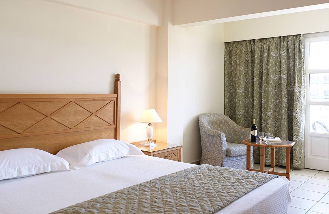 Schlafzimmer im Mitsis Petit Palais Beach Hotel mit Bett, Lampe und Fenster