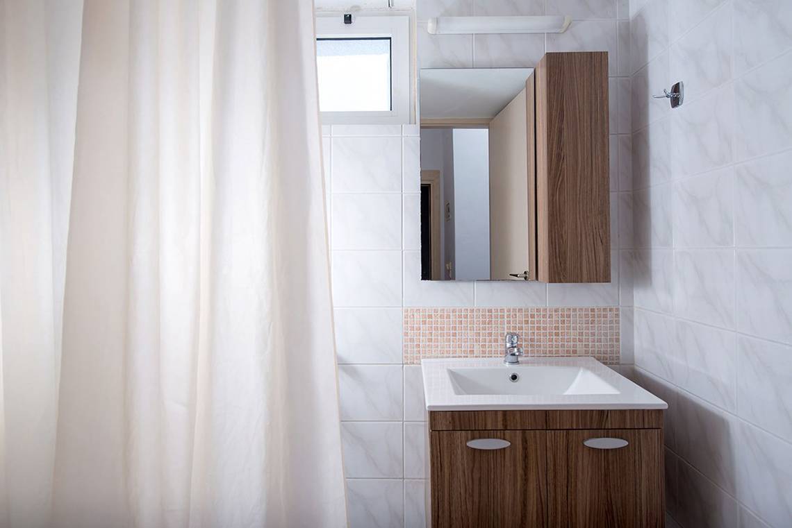 Badezimmer im Gouves Water Park Holiday Resort mit weißen Fliesen, braunem Schrank und einem Spiegel.