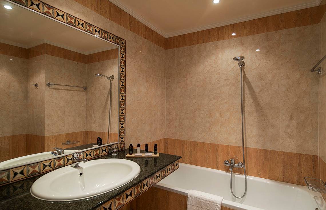 Badezimmer im Mitsis Petit Palais Beach Hotel mit Badewanne, Waschbecken und Spiegel.