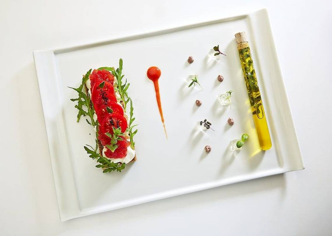 Gerichteter Teller mit Tomaten, Rucola und Öl auf weißem Hintergrund