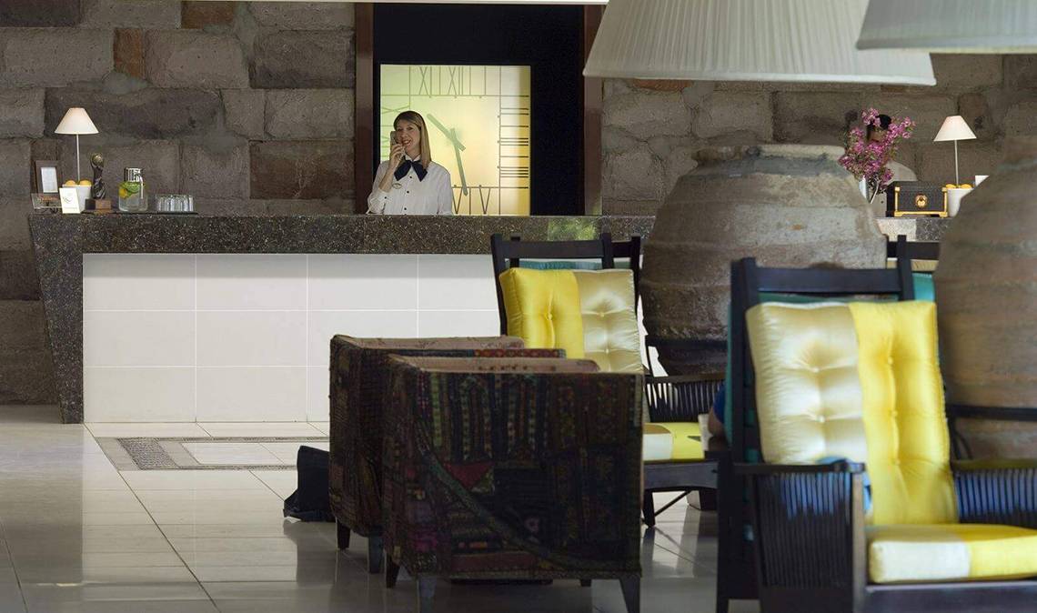 Empfangsbereich im Marmara Bodrum Hotel mit Rezeptionistin am Telefon und dekorativ eingerichteten Möbeln.