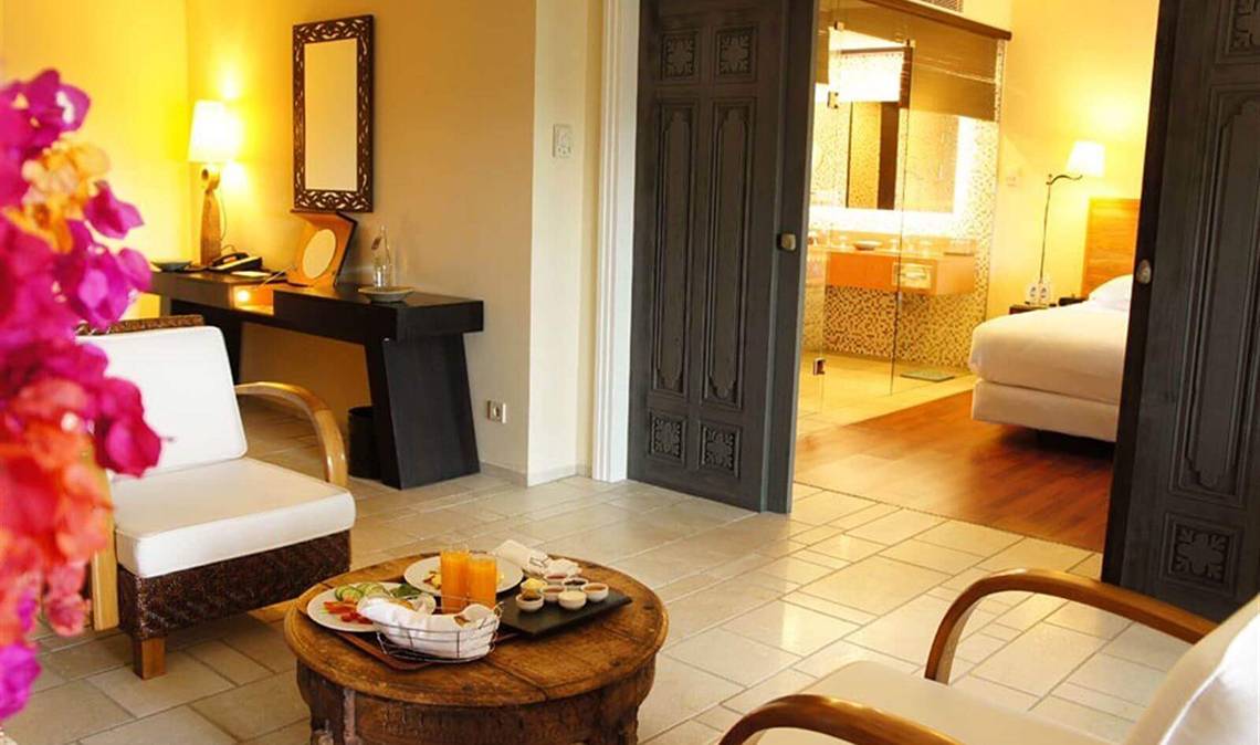 Hotelzimmer im Marmara Bodrum mit Esstisch, Sessel, Tischlampe und Schlafzimmer.