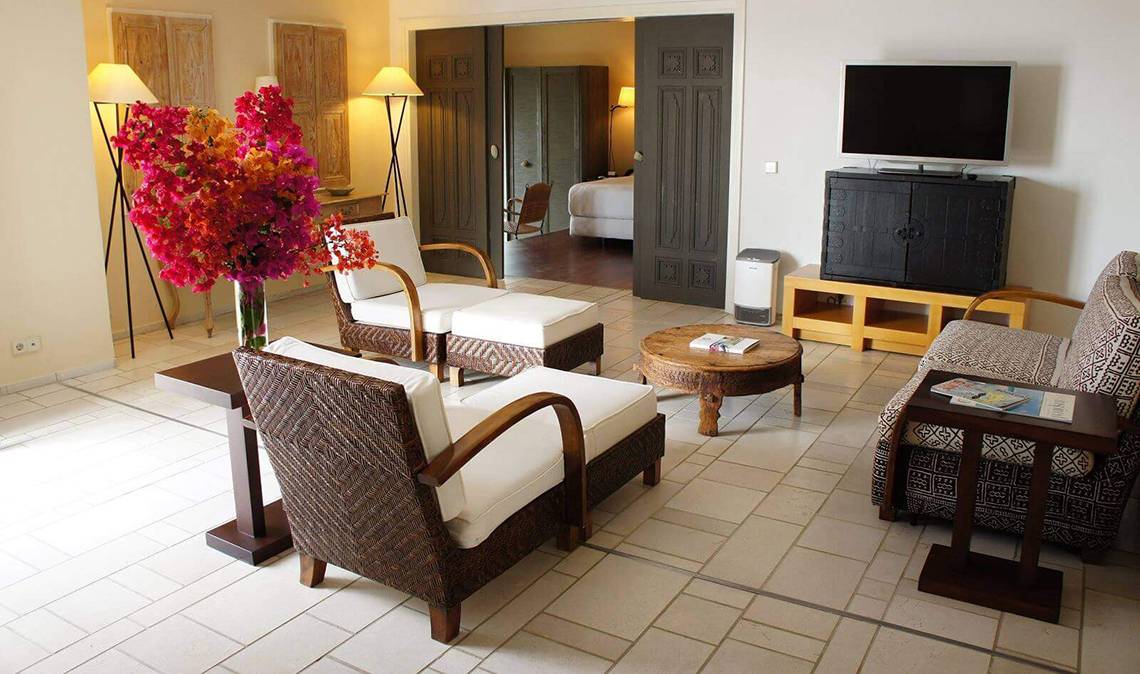 Das Wohnzimmer im Marmara Bodrum Hotel mit Fernseher, Sofa, Tisch, Blumen und Betten.