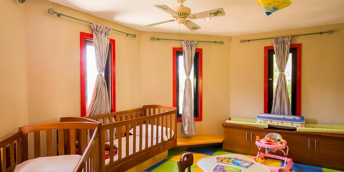 Kinderzimmer im InterContinental Resort Mauritius mit zwei Babybetten, Deckenventilator und bunten Teppich.