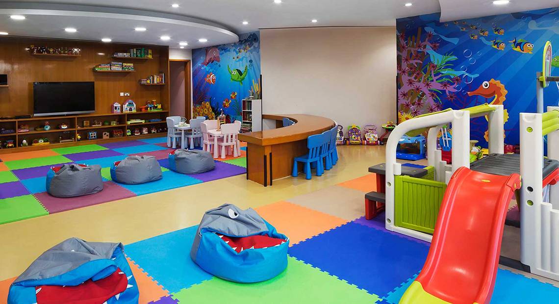 Kinderspielzimmer im Dukes The Palm, a Royal Hideaway Hotel mit bunten Teppichen, Spielsachen und einem blauen Wandbild.