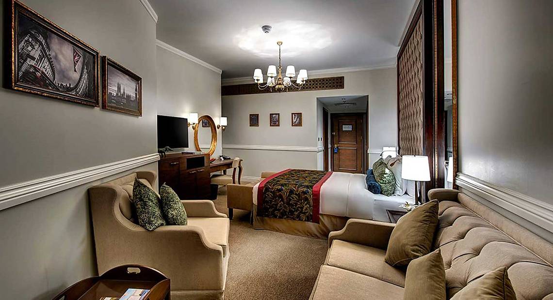 Innenansicht einer Suite im Dukes The Palm, a Royal Hideaway Hotel mit Bett, Wohnzimmerbereich und Fernseher.