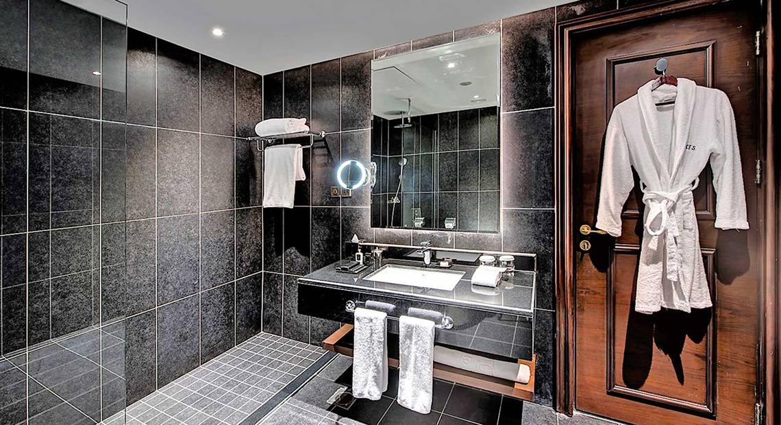 Badezimmer im Dukes The Palm, einem Royal Hideaway Hotel mit schwarzen Kacheln, einer Glasdusche und einem Waschbecken.