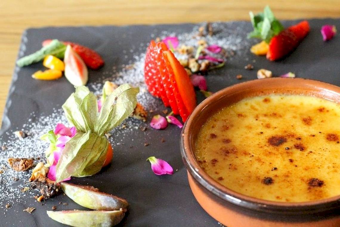 Eine Schüssel Creme Brulee mit gegarten Früchten und Dekor auf einem schwarzen Teller.