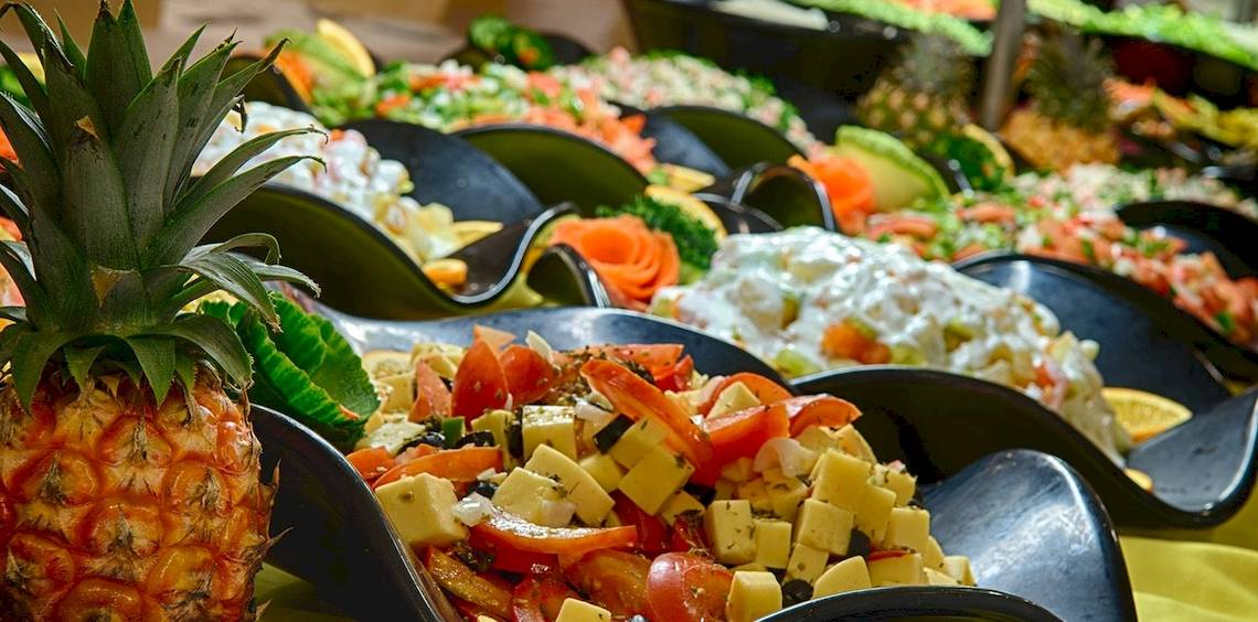 Ein Buffet mit verschiedenen Obstsalaten und Gemüseplatten, darunter ein großer Ananas-Schnitt.