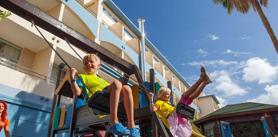 Zwei Kinder spielen auf einer Schaukelanlage im Freien vor dem IFA Altamarena Hotel.