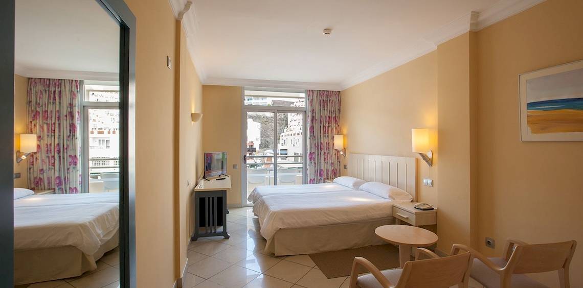 Zimmer im IFA Altamarena by Lopesan Hotels mit zwei Betten, Schreibtisch, Fernseher und Balkon.