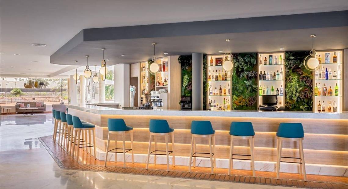 Bar im Barcelo Corralejo Bay Hotel mit grüner Wand, vielen Flaschen und blauen Stühlen