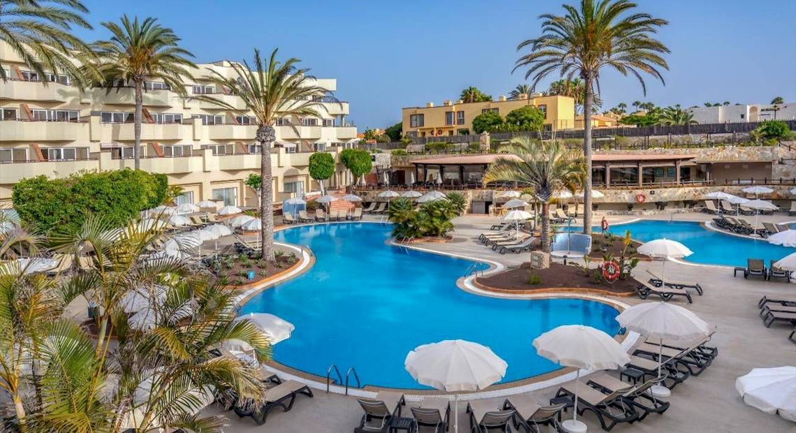 Außenansicht des Pools im Barcelo Corralejo Bay Hotel mit Sonnenschirmen und Liegestühlen.