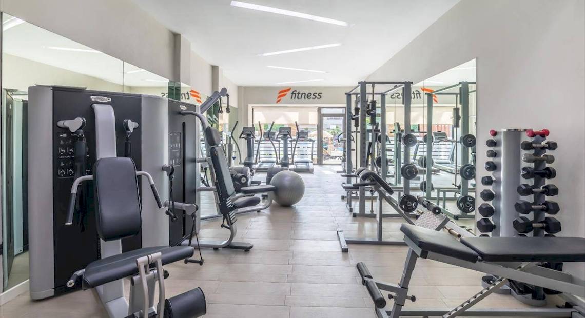 Fitnessbereich im Barcelo Corralejo Bay Hotel mit verschiedenen Trainingsgeräten und Spiegeln.