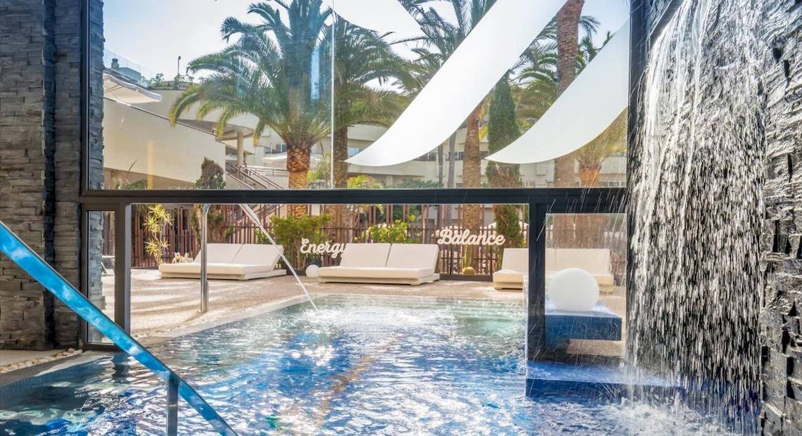 Außenpoolbereich des Barcelo Corralejo Bay Hotels mit Wasserfall und Loungemöbeln.