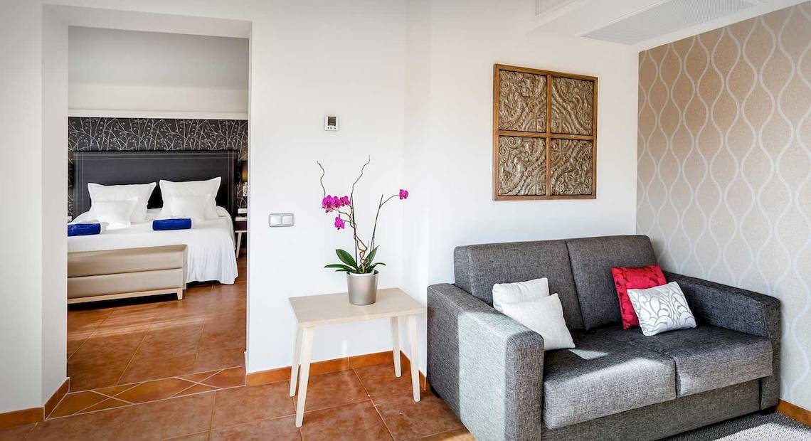 Innenansicht eines Zimmers im Barcelo Corralejo Bay Hotel mit Bett, Sofa, Tisch und Kunstwerk an der Wand.