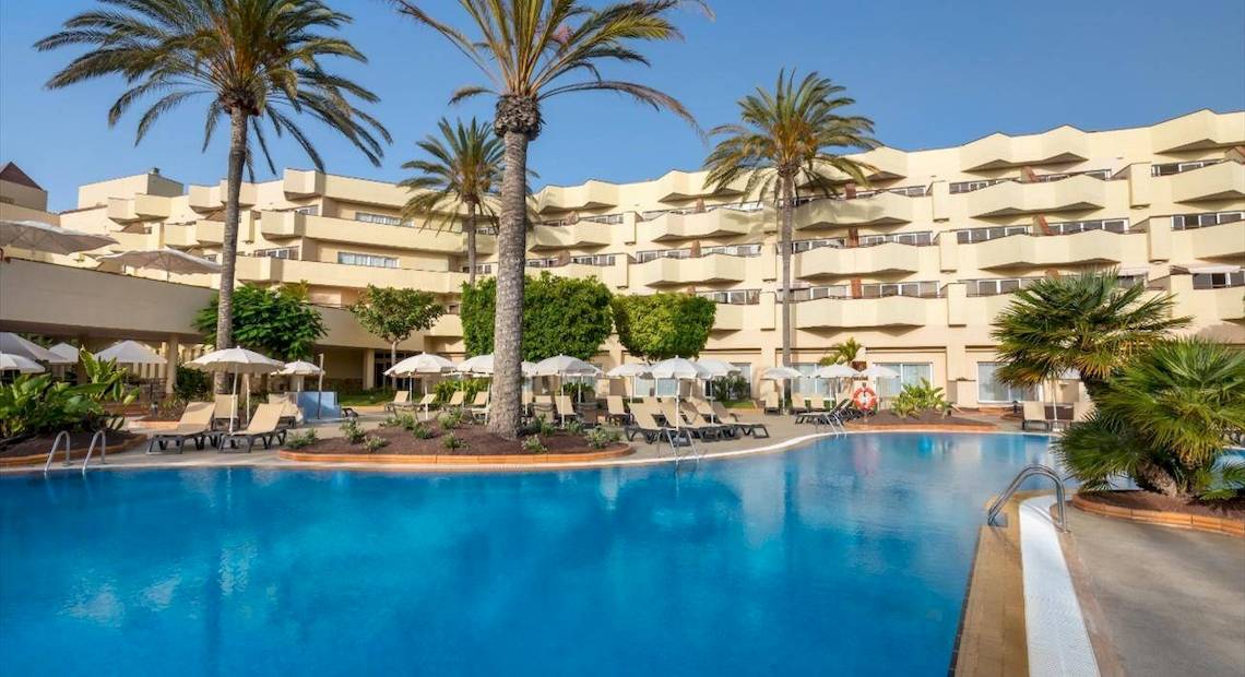 Außenbereich des Barcelo Corralejo Bay Hotels mit Swimmingpool, Sonnenliegen und Palmen