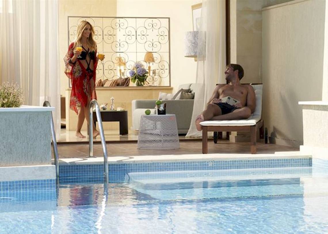 Eine Frau mit einem Glas und ein Mann in einem Liegestuhl neben dem Pool im Atlantica Imperial Resort & Spa.