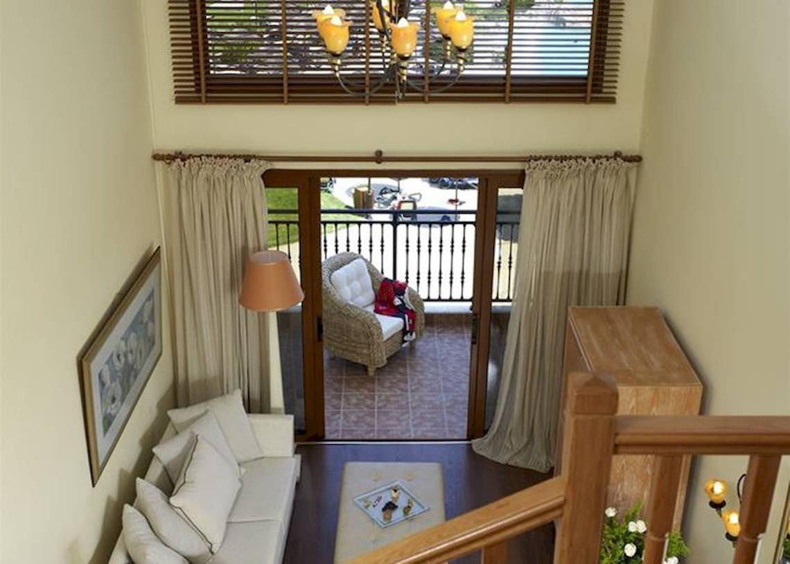 Innenansicht eines Wohnzimmers mit Balkon im Atlantica Imperial Resort & Spa, das eine weiße Couch, ein Beistelltischchen, eine Lampe und ein Fenster zeigt.