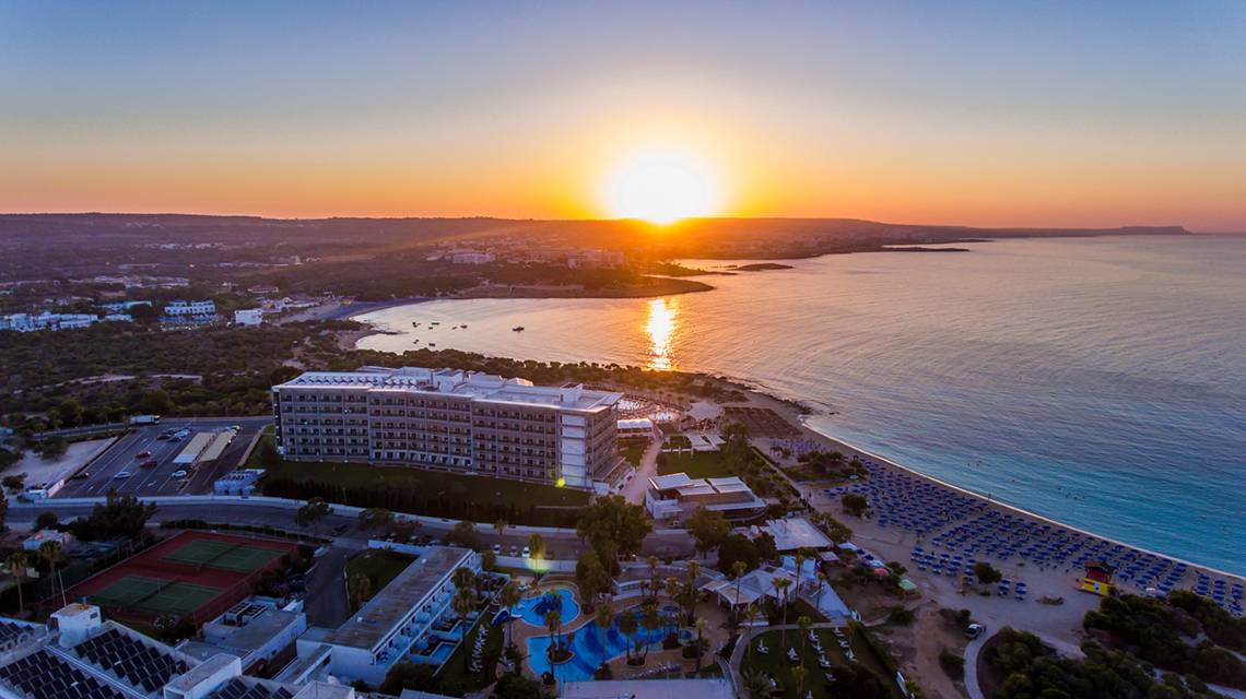 Luftaufnahme des Asterias Beach Hotels bei Sonnenuntergang mit Blick auf das Meer und die Küste