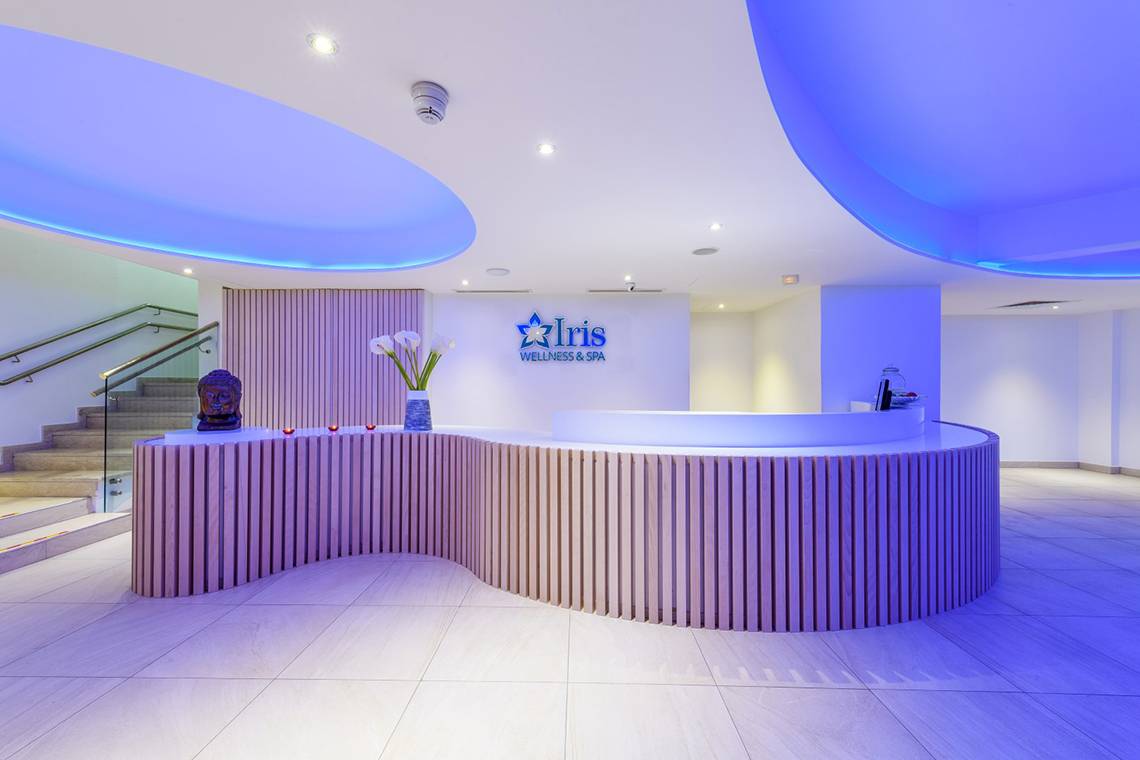 Rezeption des Wellness- und Spa-Bereichs im Asterias Beach Hotel mit violetten Beleuchtung und Empfangstresen.