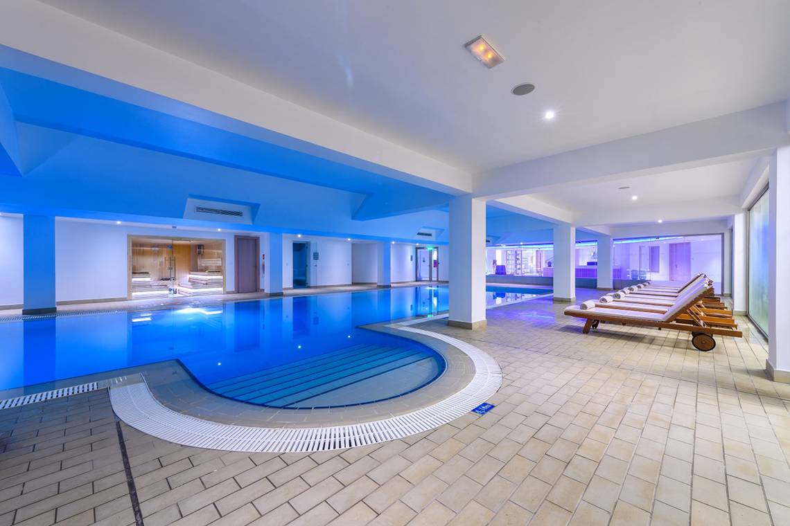 Innenpool des Asterias Beach Hotels mit blauen Lichtern und Liegestühlen.