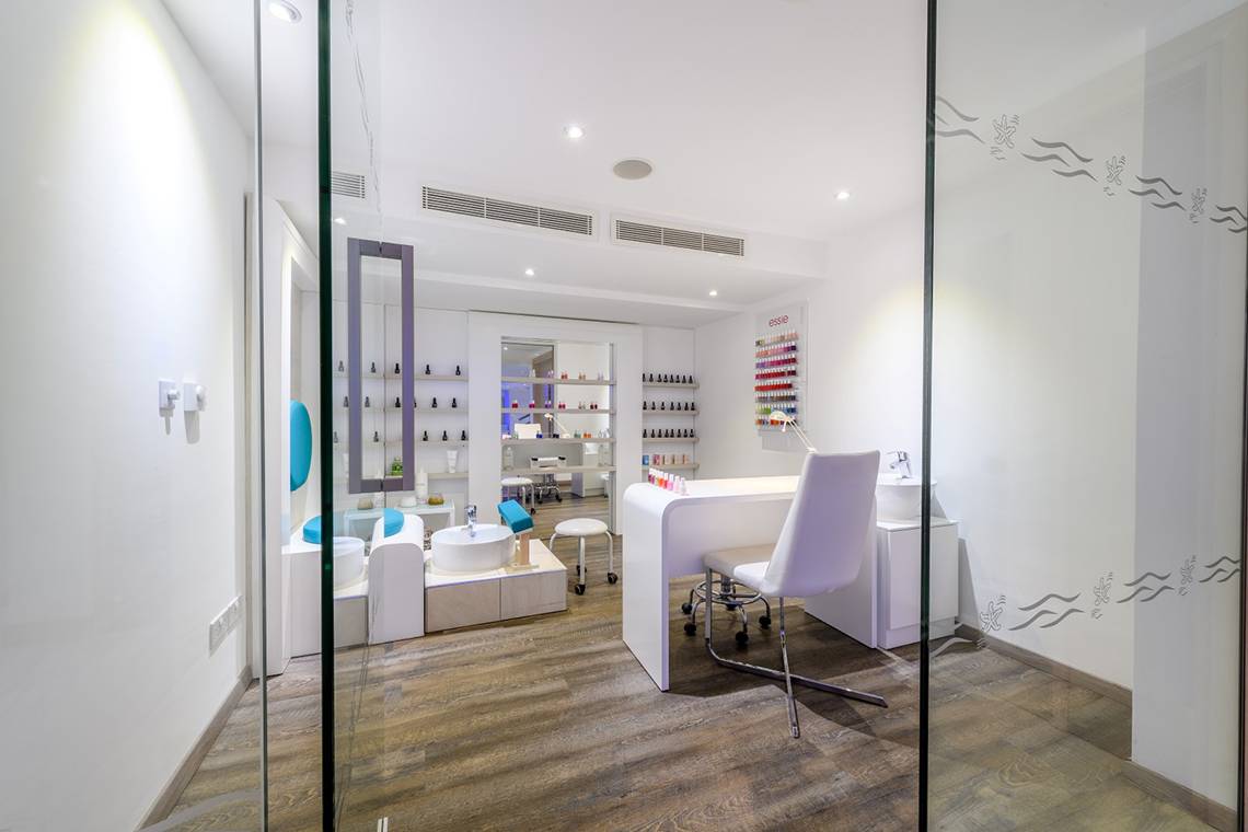 Innenansicht des Nagelstudios im Asterias Beach Hotel mit weißen Möbeln und Holzboden.