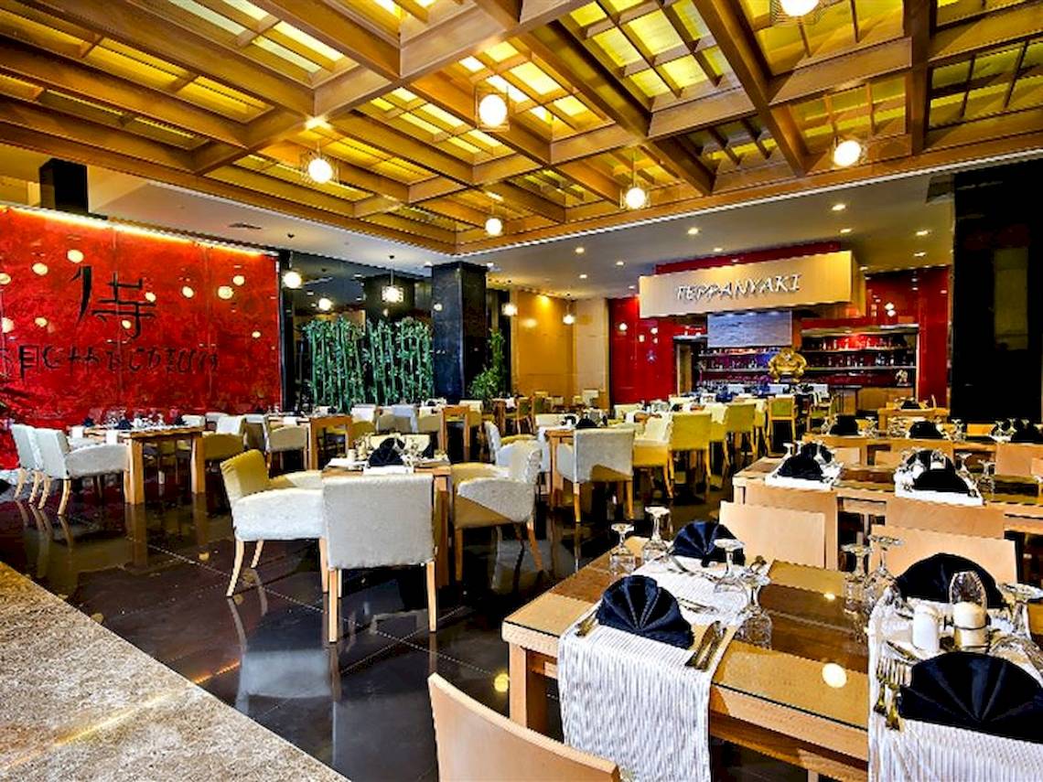 Innenansicht des Restaurants im Serenity Alma Heights Hotel mit gedeckten Tischen und hängenden Lampen.