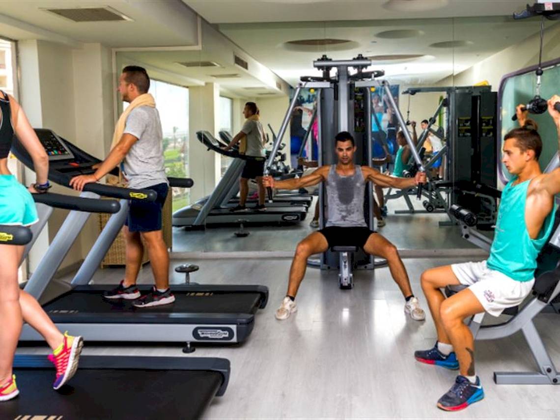Fitnessstudio im Serenity Alma Heights Hotel mit Personen, die an Geräten trainieren.