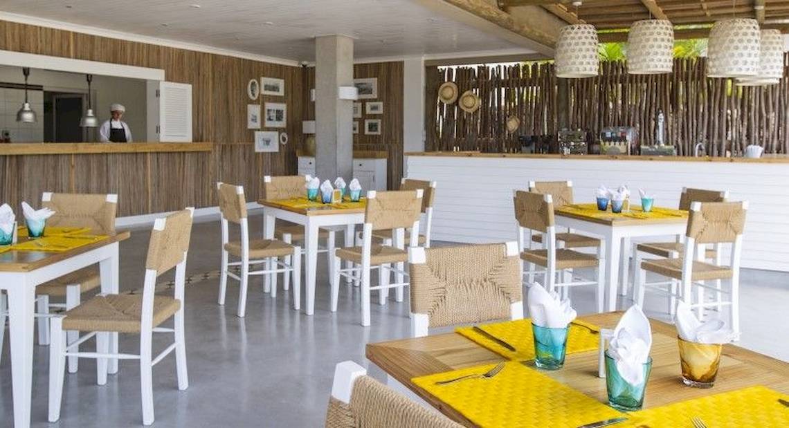 Innenbereich des Zilwa Attitude Hotels mit weißen und gelben Tischen, braunen Stühlen und Holzwänden.