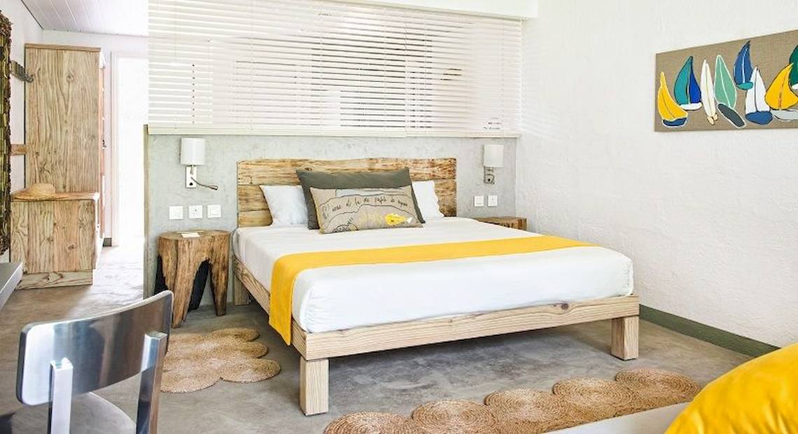 Ein modernes Hotelzimmer im Zilwa Attitude mit weißem Bett, gelber Decke, Holzbettrahmen, Nachttischen und Wanddekoration.