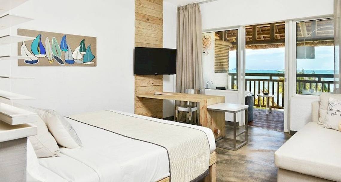 Ein modernes Hotelzimmer mit einem Bett, Schreibtisch, Fernseher und einem Balkon mit Meerblick.