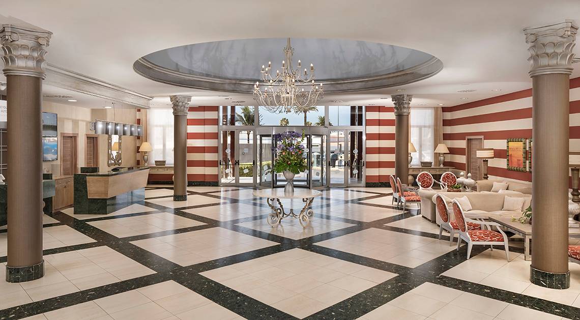 Foyer des HD Parque Cristobal Hotels mit Kronleuchter, schwarzen und weißen Fliesen, roten und weißen Streifen und Möbeln.
