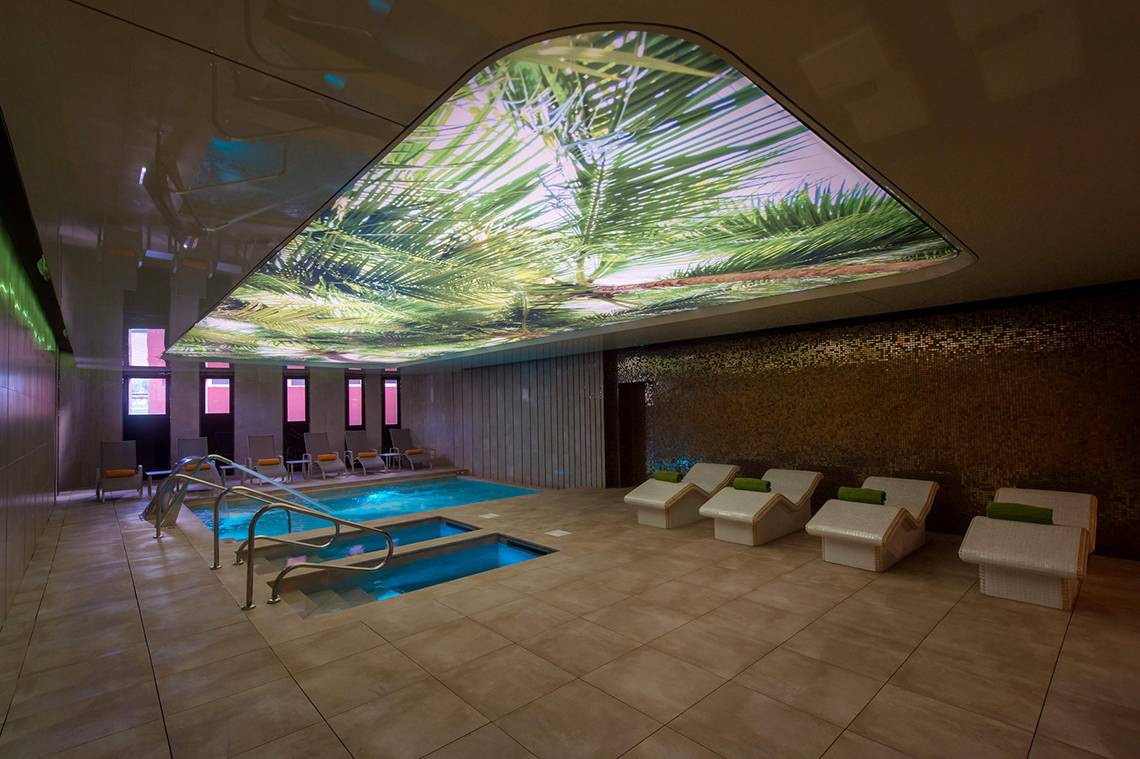 Innenpool im HD Parque Cristobal mit Palmenprojektion an der Decke und Liegen.