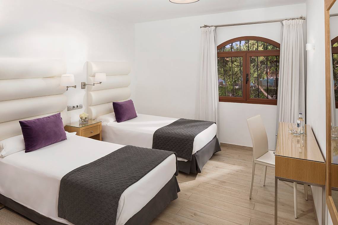 Innenansicht eines Hotelzimmers im HD Parque Cristobal mit zwei Betten, weißem Dekor und einem Fenster.