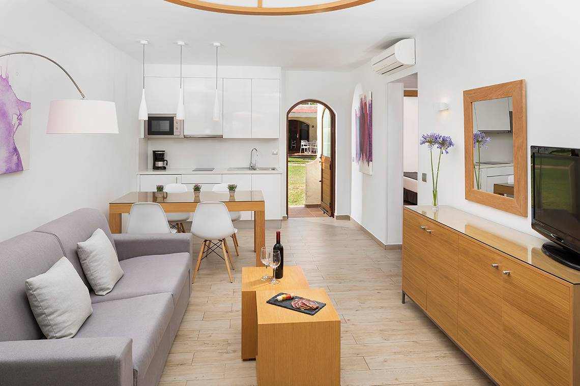 Wohnbereich des HD Parque Cristobal Hotels mit Sofa, Tisch, Weinflasche und Fernseher.