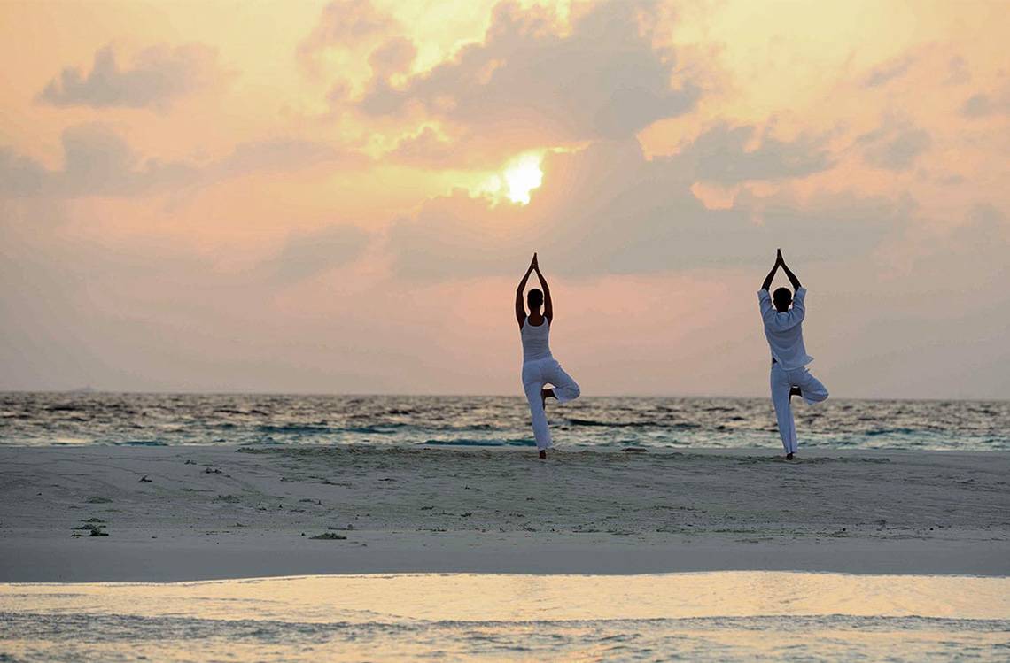 Zwei Personen machen Yoga am Strand bei Sonnenuntergang am Baros Maldives Resort.
