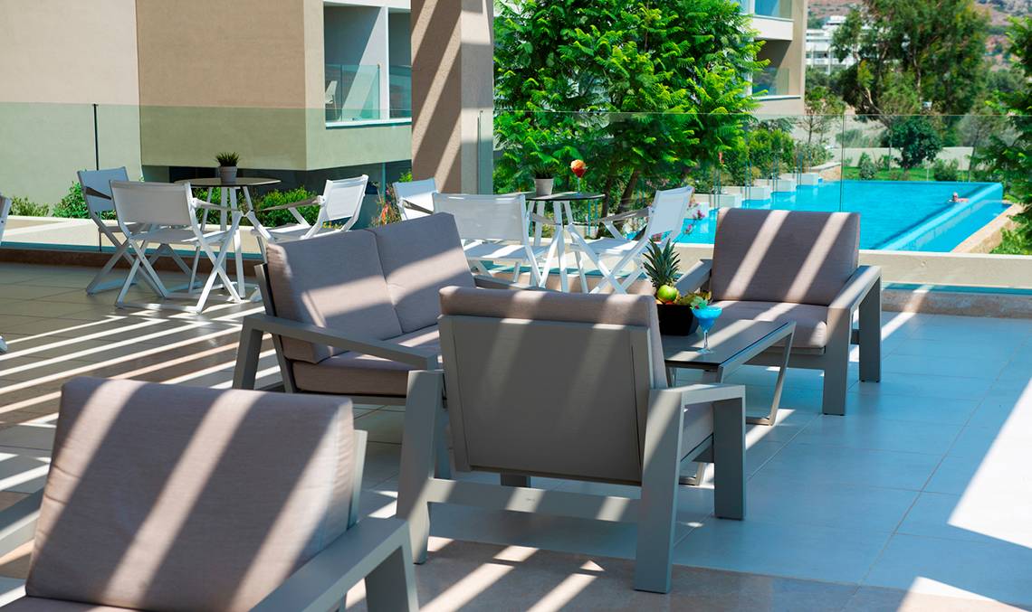 Lounge-Terrasse im Amada Colossos Resort mit Sitzmöbeln und Swimmingpool im Hintergrund.