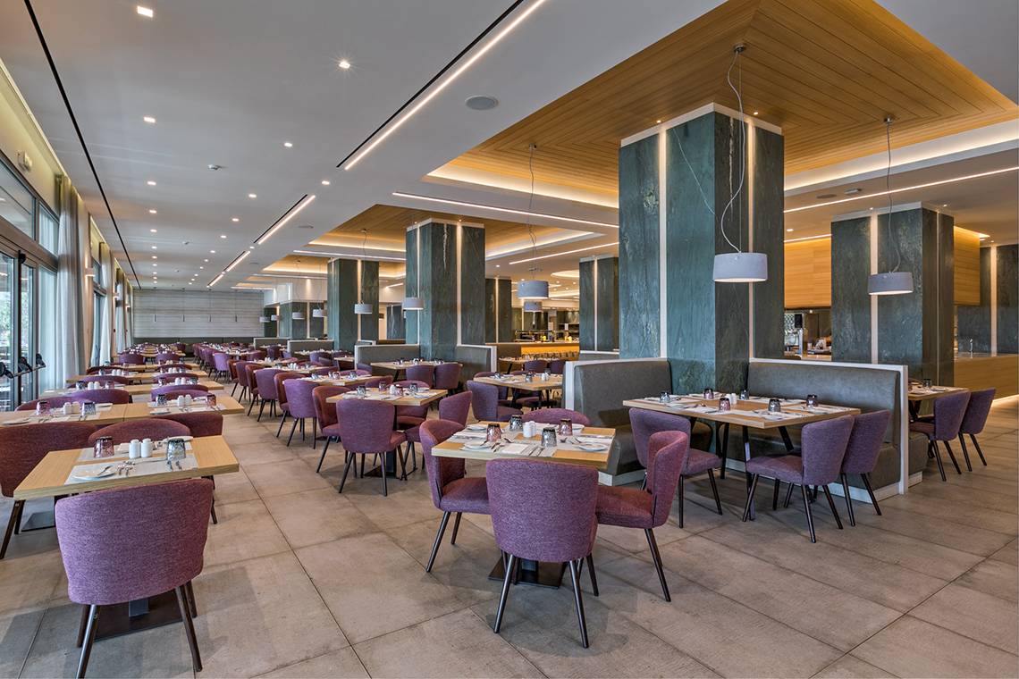 Restaurant des Amada Colossos Resorts mit vielen Tischen und Stühlen, hoher Decke und Marmorsäulen.