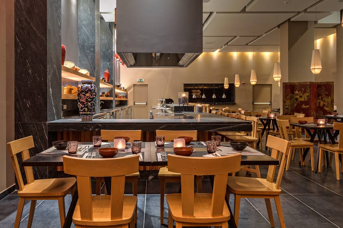 Innenbereich des Restaurants im Amada Colossos Resort mit Holztischen, Stühlen und einer Theke.