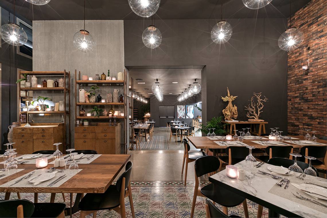 Innenansicht des Restaurants im Amada Colossos Resort mit Holztischen, schwarzen Stühlen und dekorativen Gegenständen.