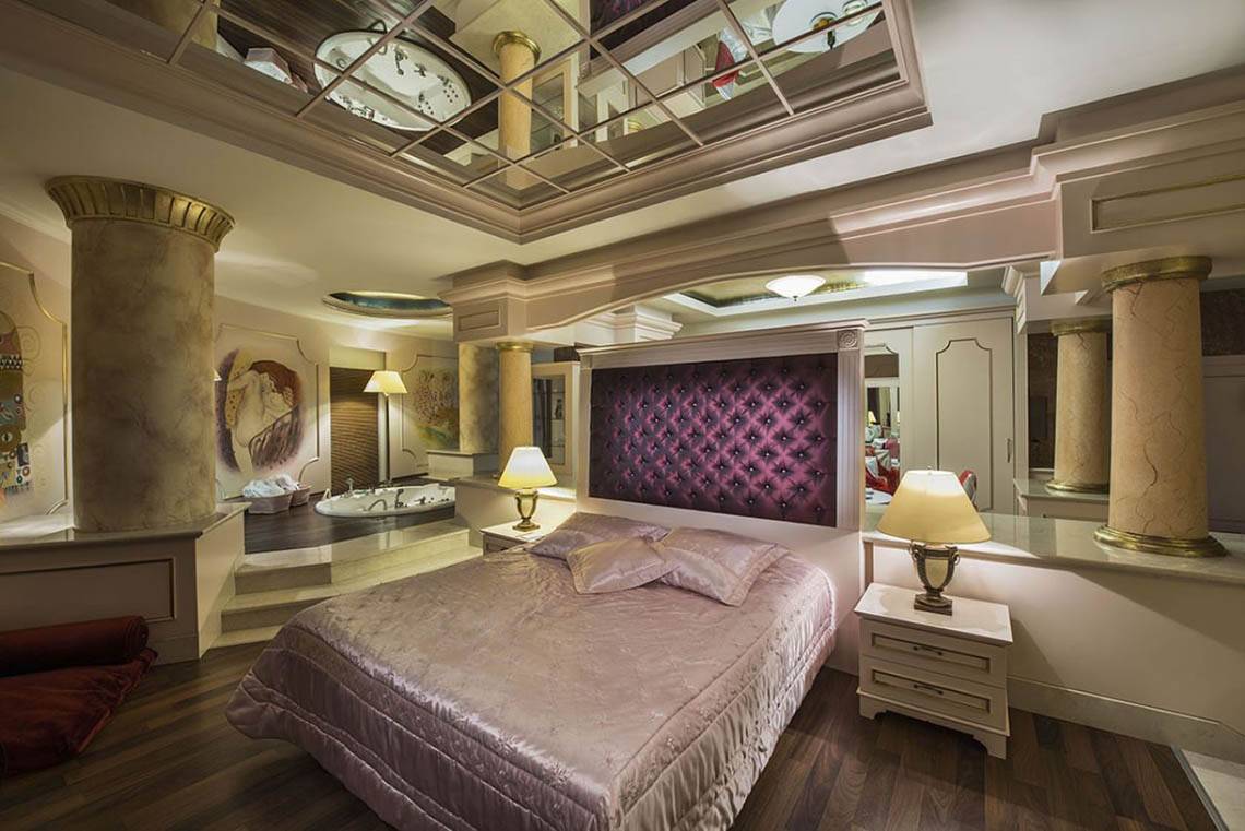 Schlafzimmer im Delphin Diva Premiere Hotel mit Bett, Nachttischen, Lampen und Badewanne