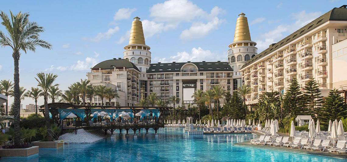 Außenansicht des Delphin Diva Premiere Hotels mit Swimmingpool, Brücke und Sonnenliegen.