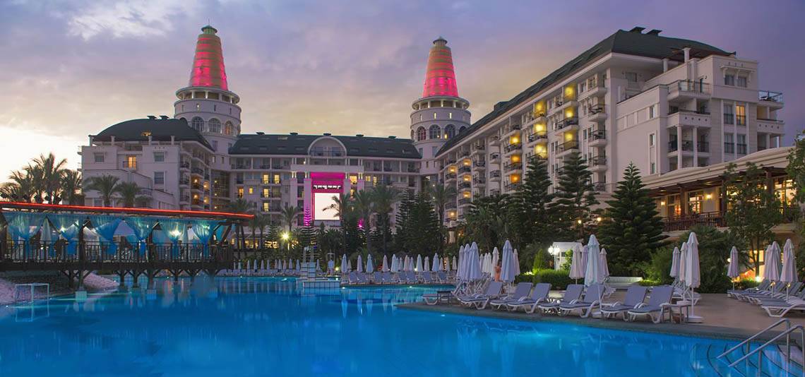 Das Delphin Diva Premiere Hotel mit beleuchteten Türmen und Swimmingpool im Abendlicht.