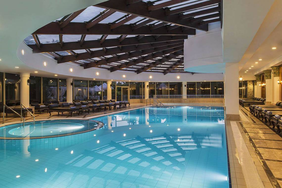 Innenpool des Delphin Diva Premiere Hotels mit Liegestühlen und Glasdach.