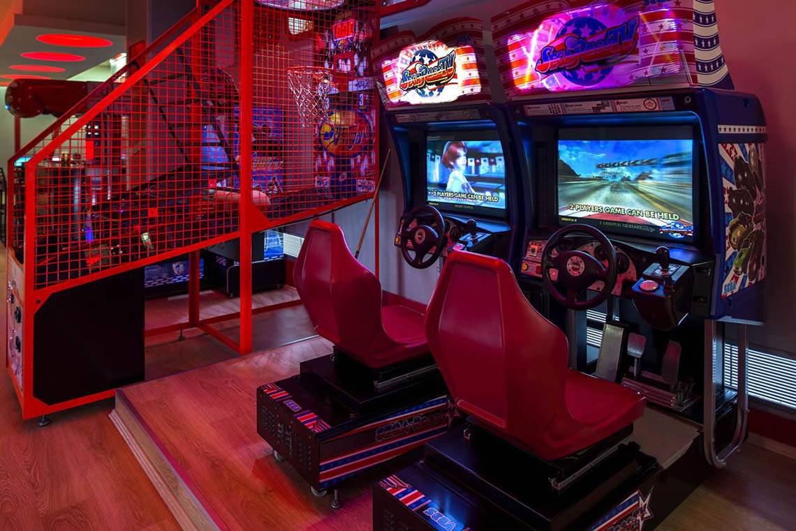 Arcade-Spielebereich im Delphin Diva Premiere Hotel mit zwei roten Sitzen und Monitoren.