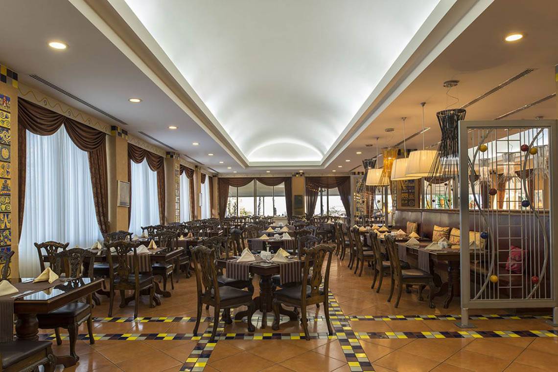 Innenansicht des Restaurants im Delphin Diva Premiere Hotel mit runden Tischen, Stühlen und dekorativen Wandmustern.